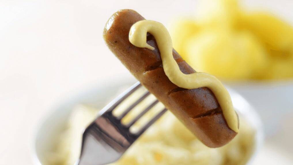 vegane Wurst mit Senf auf einer Gabel