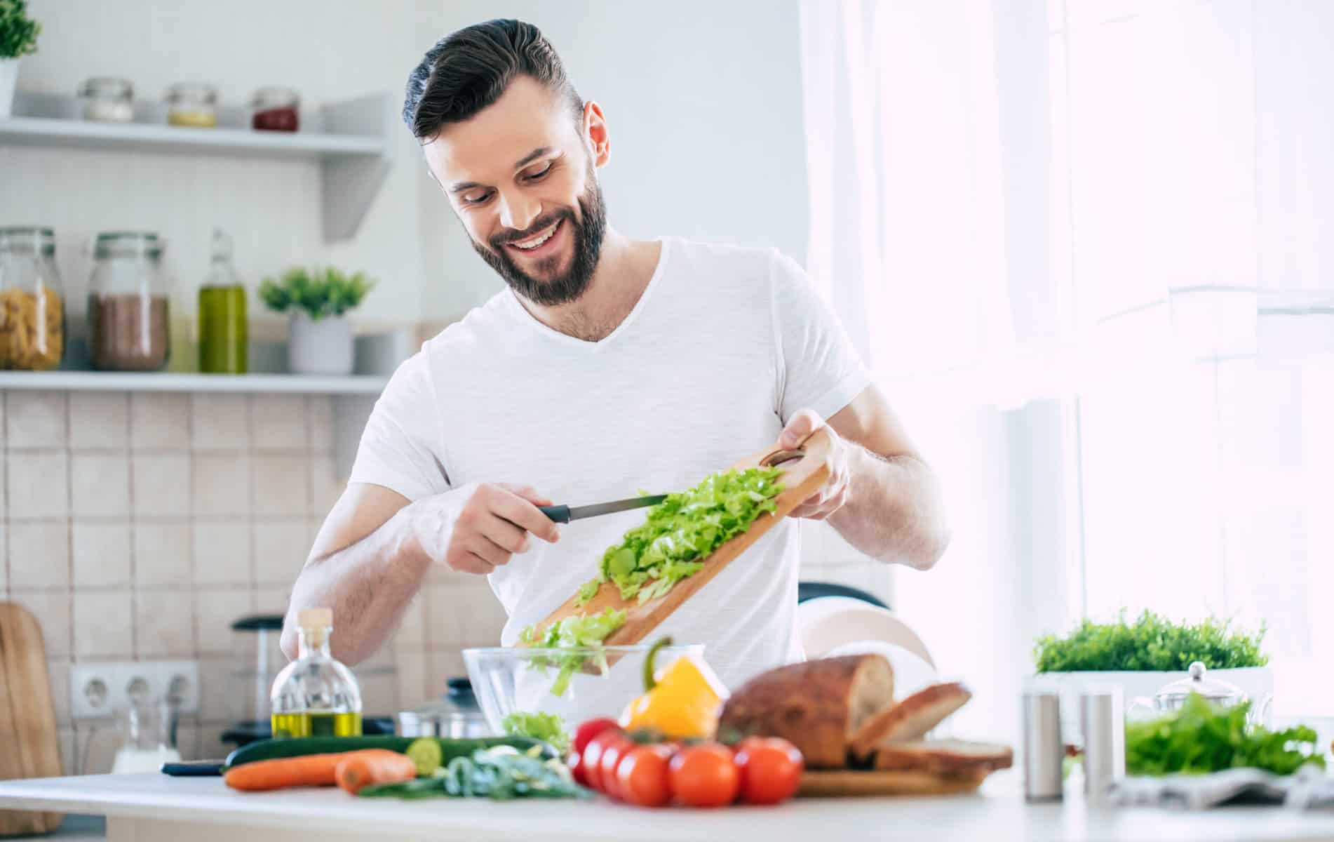 A men cutting vegetables ion a wooden board in a kitchen
